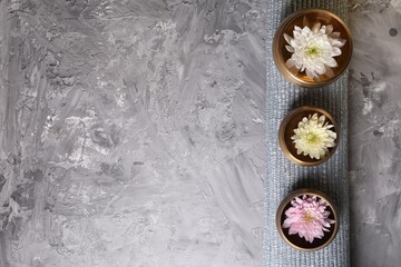 Tibetan singing bowls with water, beautiful chrysanthemum flowers on grey textured table, top view....