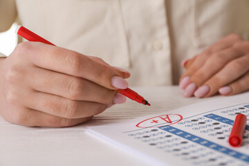 School grade. Teacher writing letter A with plus symbol on answer sheet at white table, closeup