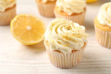 Tasty cupcakes with cream, lemon zest and fruit on white wooden table, closeup