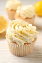 Tasty cupcake with cream and lemon zest on white wooden table, closeup