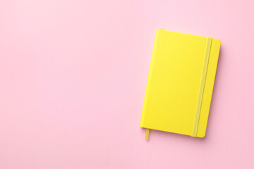 Closed yellow notebook on light pink background, top view. Space for text