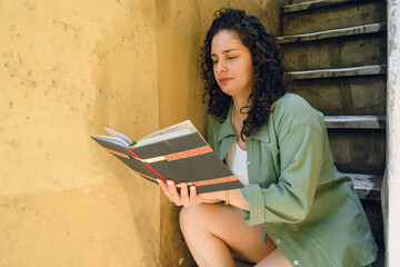 young latin woman student at home sitting on stairs reading reviewing her college notes