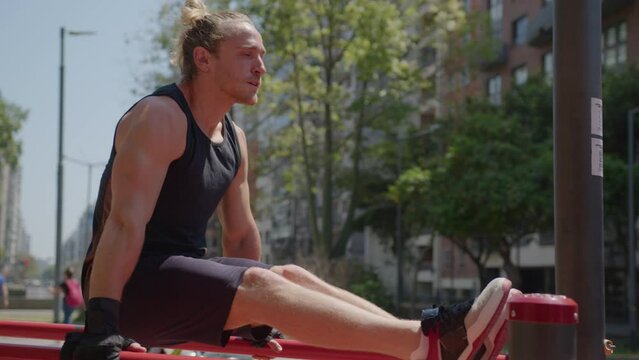Muscular man in sports clothing doing l-sit tricep dips on parallel bars during outdoor fitness workout at street gym