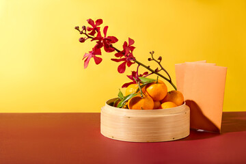 Tangerines are stored in a bamboo steamer, next to a fresh orchid branch and a lucky money...