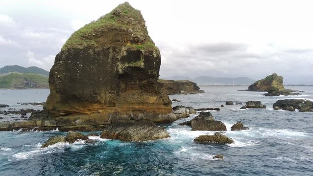 Drone shot on Papuma Beach, Jember, Indonesia with thick vegetations, towering cliff and ocean waves.