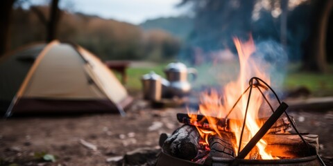 A Camp fire and a tea pot are foreground and focused, there is a tent in the background and defocused copy space 