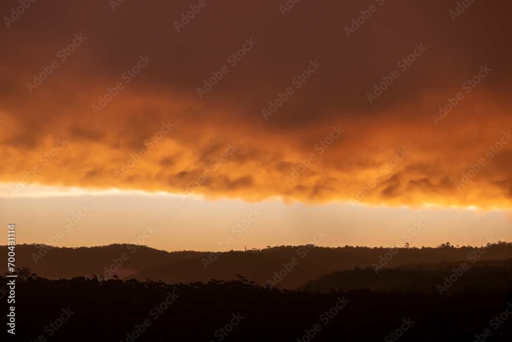 Wall mural Photograph of a bright orange sunset sky over a large valley after a thunderstorm in The Blue Mountains in New South Wales in Australia