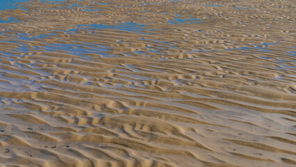 The seabed exposed at low tide. Pools of blue water formed between the wavy sandy ridges. Close-up. Full screen. Madagascar. Morondava. Mozambique Channel
