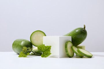 A white cube placed on white surface with green leaves and winter melon slices. Glamour minimal...