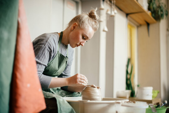 Young woman potter moulding the walls of a clay ware on a potter's wheel A woman potter at work, making pottery