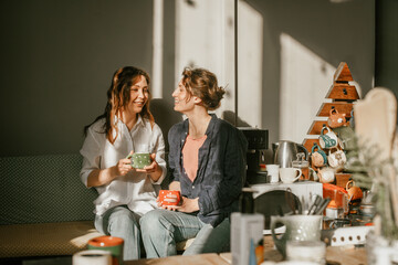 Two female friends enjoying morning coffee in a cozy home kitchen Sunny morning and friendly...