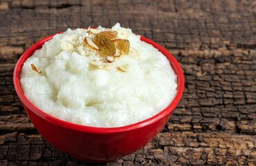 Payesh or Payasam Garnished with Cashew, Raisin, Almond in a Red Bowl Isolated on Wooden Background with Copy Space, Also Known as Ksheeram, Milk Rice Pudding, Kheer or Rice Payesh