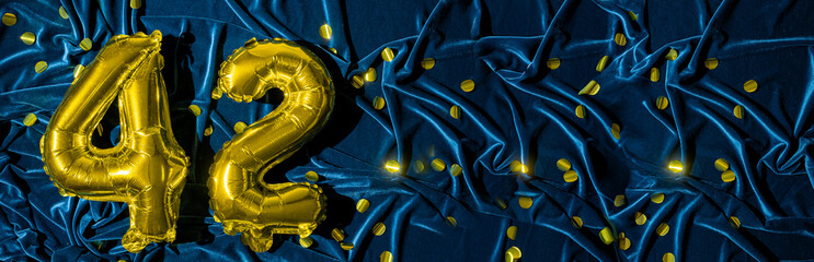 number forty two, gold foil balloon number on a blue velvet background with confetti. Birthday...