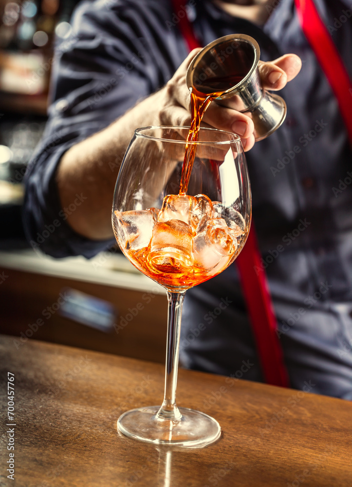 Wall mural the barman in the bar prepares a summer cocktail spritz veneziano, pours aperol liqueur into a glass