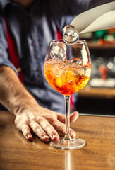 The bartender at the bar prepares the summer cocktail Spritz Veneziano, adds ice cubes to the drink