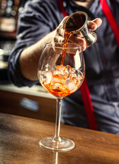 The barman in the bar prepares a summer cocktail Spritz Veneziano, pours Aperol liqueur into a...