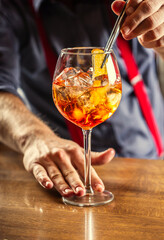 The bartender in the bar prepares the summer cocktail Spritz Veneziano, adds a slice of orange to...
