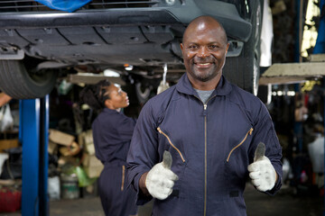 mechanic smiling and thumbs up pose in automobile repair shop