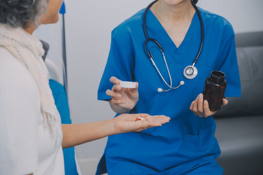 Asian woman nurse holding a medicine bottle and telling information to Asian senior woman before administering medication. Caregiver visit at home. Home health care and nursing home concept.