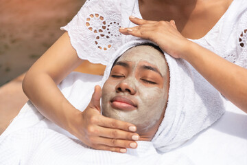 Young African American black woman lies down while a facialist uses facial cream and mask to...