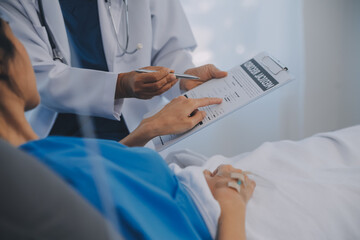 The senior woman specialist doctor with stethoscope checking up happy young Asian female patient lying in bed with receiving an intravenous saline drip in recovery room. Healthcare, medical insurance.