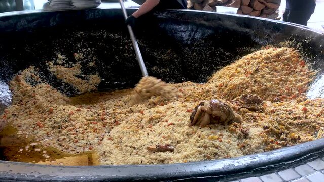 Cooking traditional uzbek plov that is made of rice and meat on a big plot mixing with big spoon 