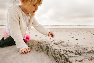 Young girl child building a sand castle on beach under stormy sky