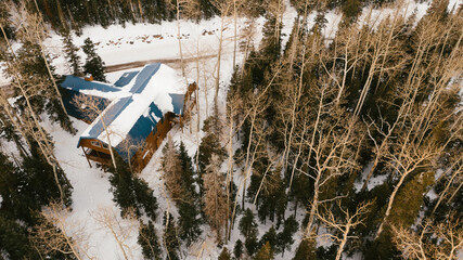 Drone view of snow covered cabin and trees in mountains