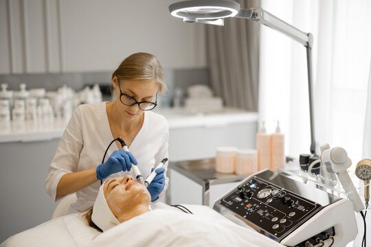Young beautician doing microcurrent therapy on a client's face in beauty salon. Concept of cosmetology procedures for facial care. Portrait of a medical cosmetologist at work