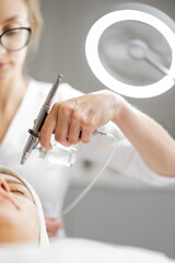 Young cosmetologist performs oxygen mesotherapy on woman's face at beauty salon. Concept of non-invasive and revitalizing skin treatment - obrazy, fototapety, plakaty