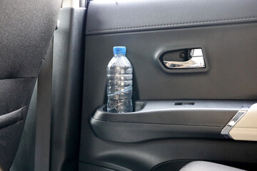cup holder in car. a plastic drinking bottle tucked into the bottle coaster on the car door. car interior. availability of drinks while driving.
