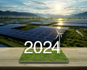2024 white text with wind turbine on green grass on open book on wooden table over solar photovoltaics farm located on mountain and sunrise, Happy new year 2024 ecological cover concept