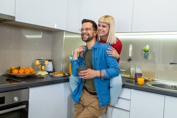 Young man and woman standing in kitchen and talking. Happy wife and husband with cups of coffee and juice standing in the kitchen.