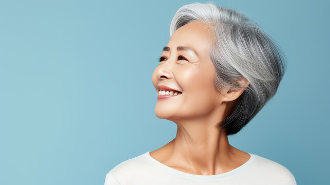 Elegant, smiling, elderly, chic Asian woman with gray hair and perfect skin on a light blue background banner.