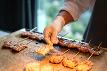 Action of a chef is grilling pork skewer on the cooking pan. Food cooking scene photo, selective focus. - obrazy, fototapety, plakaty
