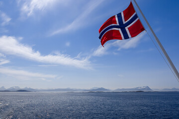 A vivid Norwegian flag billowing against a summer sky, set over a landscape of low northern...