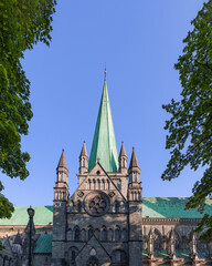 The main entrance of Nidaros Cathedral (Nidarosdomen) in Trondheim, Norway, is majestically framed by green trees on either side, highlighted by its striking pointed spire