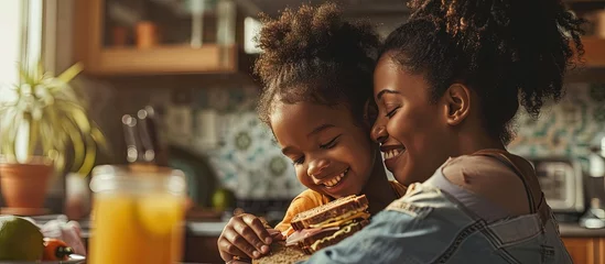 Tuinposter Loving black mother and daughter cuddling while having snack at kitchen eating healthy sandwiches and drinking orange juice happy mom embracing her hungry kid teen girl copy space. Creative Banner © HN Works