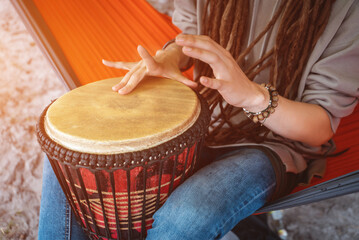 person with dreadlocks play tribal reggae at small African hand drum djembe