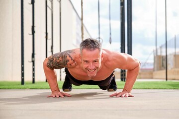 Man doing push up, smiling and looking at camera in an outdoor training gym. CrossFit, fitness and sport.