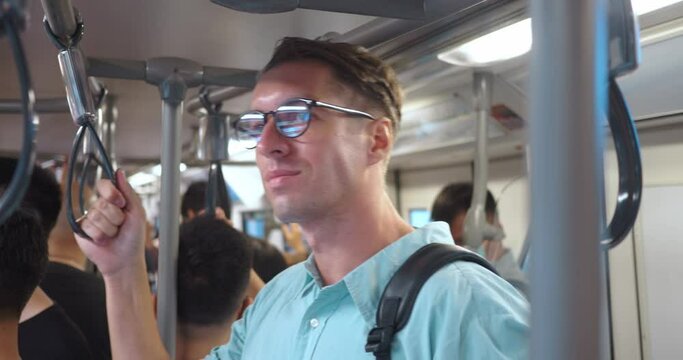 Passenger rides in crowded subway car, holding handrail. Due to large number of passengers, man has to stand, clinging to handrail. Concept of male passenger in public transport returning from work.