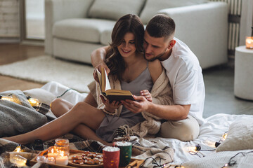 Happy young couple relaxing together in the bedroom at home, reading book. Man and woman enjoying...