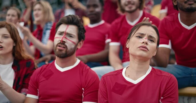 Fans with their faces painted with the English flag sit in the stands. People worrying while watching fierce football game. Having negative emotions about fail of their team. Leisure concept.
