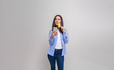 Thoughtful female customer with credit card and mobile phone looking away over white background