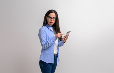Portrait of shocked businesswoman pointing at smart phone and looking at camera on white background