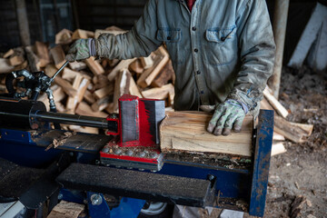 Man with work gloves cuts firewood with hydraulic log splitter closeup