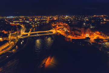 Aerial view on illuminated Galway city Cathedral and Salmon Weir Bridge and new walking bridge. Dark and warm color tone. City at night. Irish town landmark.