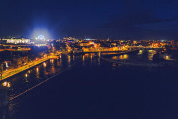 Fototapeta premium Aerial view on illuminated Galway city, Ireland. Dark sky and river Corrib. Stunning nature scene. Fun wheel glowing in the background.