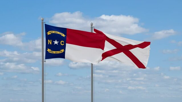 Alabama and North Carolina US state flags waving together on cloudy sky, endless seamless loop