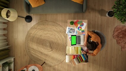 Obraz premium Top view capturing a man working in his home office. Young designer is looking through, comparing the textile color samples for his project and inserting data into his laptop.